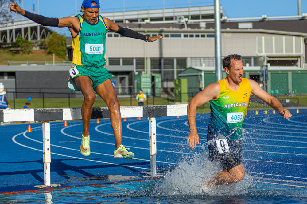 A masters athlete running through the water after clearing the water jump barrier
