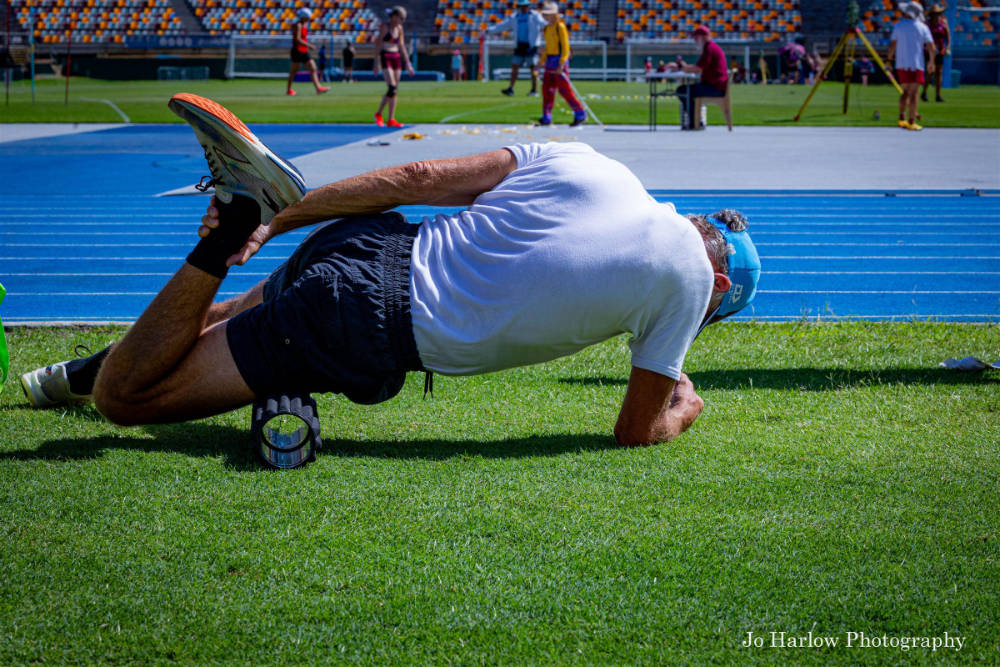 An athlete stretching on the grass beside the track, using a foam roller