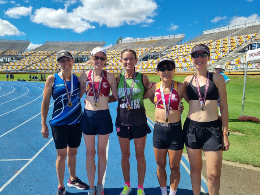 Melanie with four fellow masters athletes on the track after a 5,000m, all wearing medals