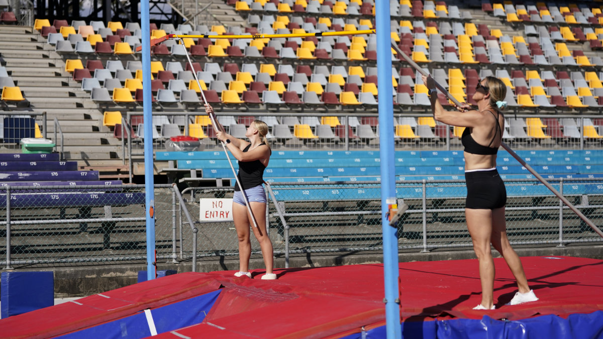 Two volunteers raising the crossbar on the pole vault standards